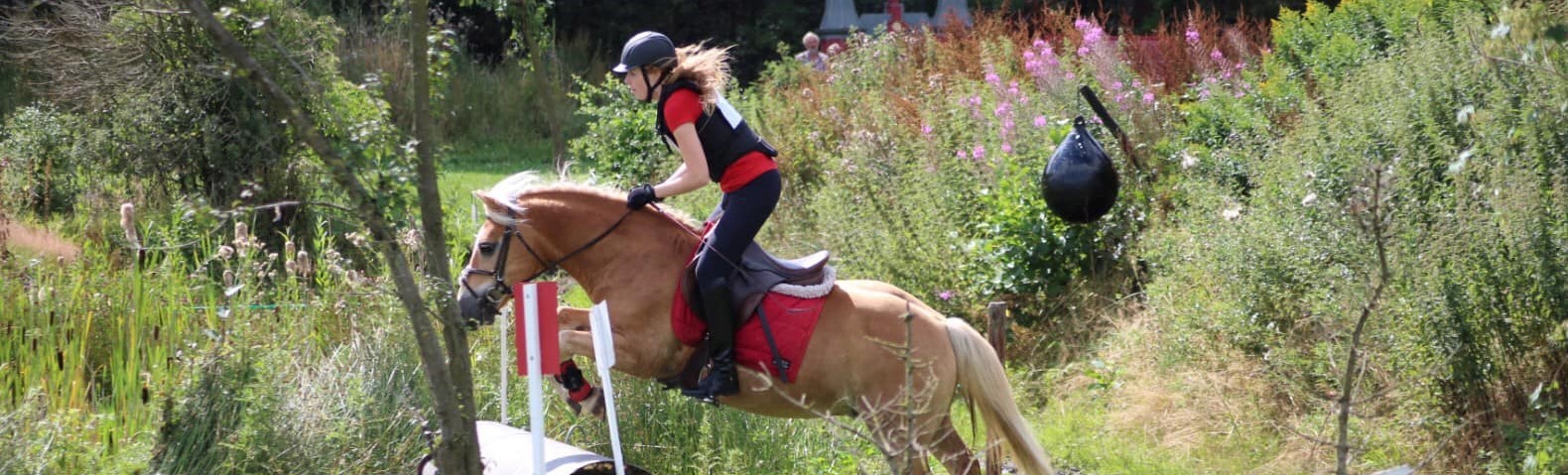Nynke springt met haar haflinger over een greppel tijdens een cross